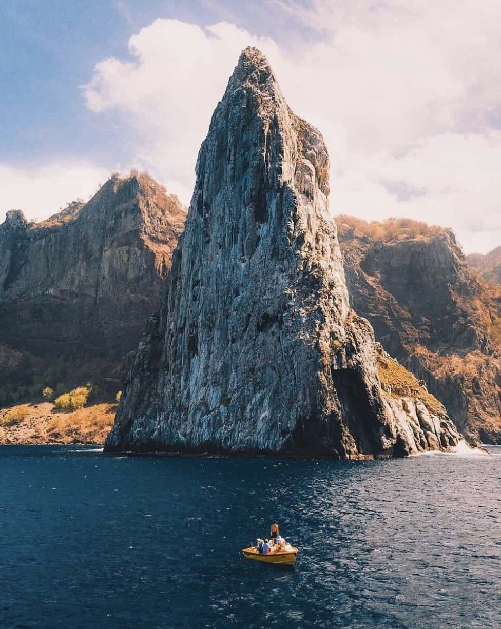 a boat in the water with a tall rock formation in the background from Ua Pou island in French Polynesia