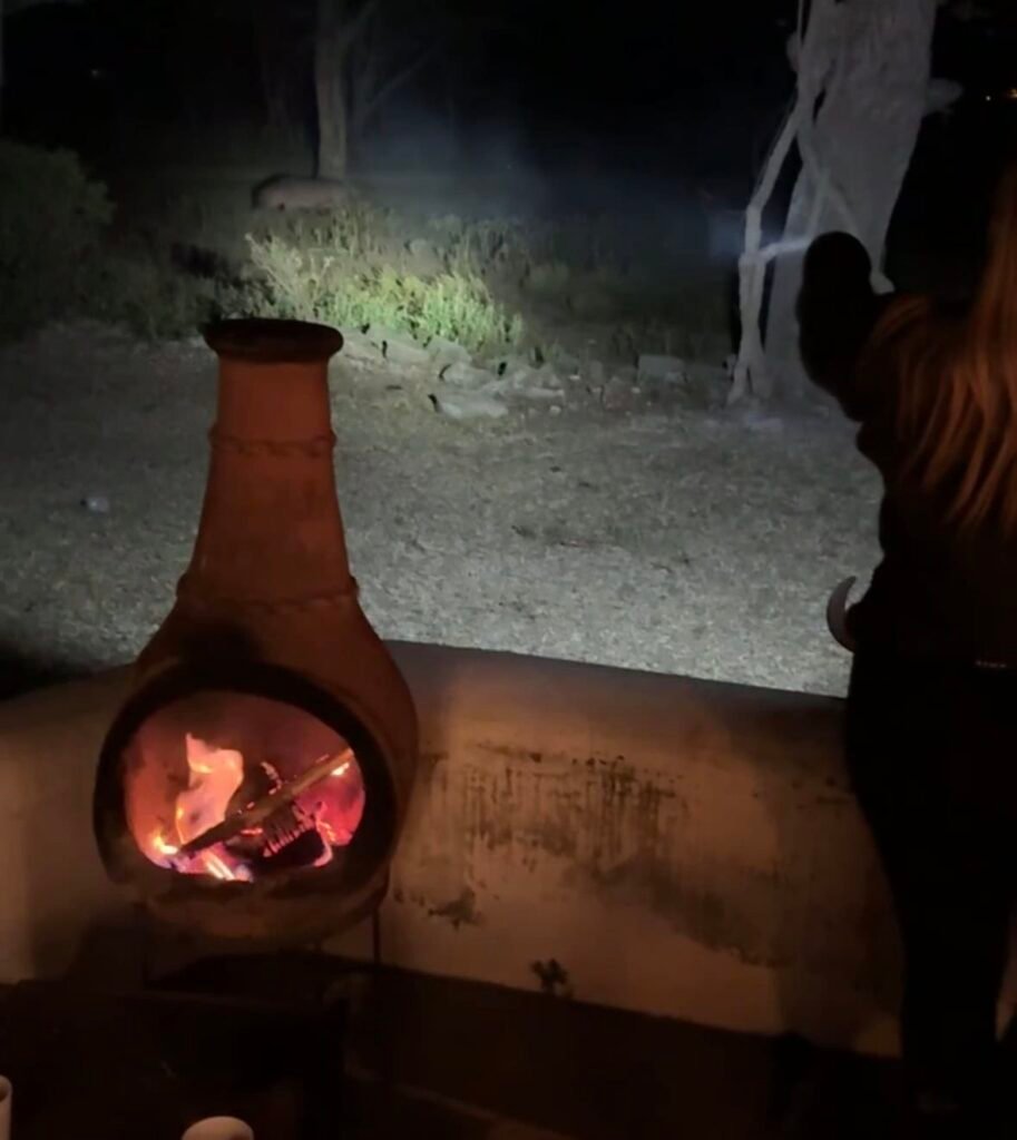 A cozy outdoor nighttime scene with a clay fireplace, warm fire burning, and a person enjoying the peaceful surroundings of nature. Perfect for reflecting and relaxing in a tranquil, rustic setting.
