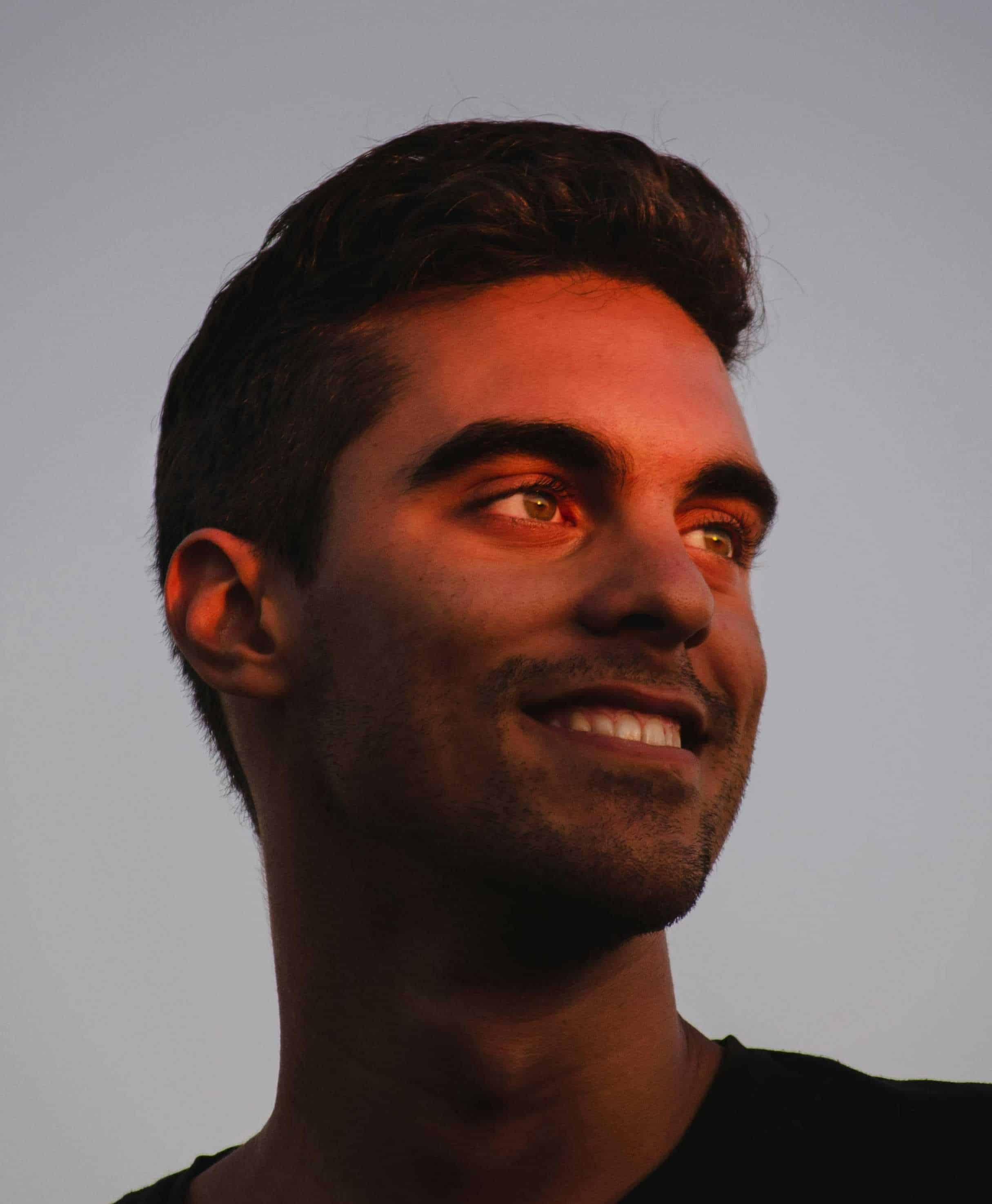 Young man smiling with sunset lighting, peaceful outdoors, clear sky background - lost between oceans theme, representing serenity, exploration, and connection with nature.