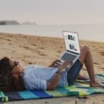 Holafly image of a person lying on a beach towerl working on her laptop in front of the sea thanks to her best eSIM for international travel