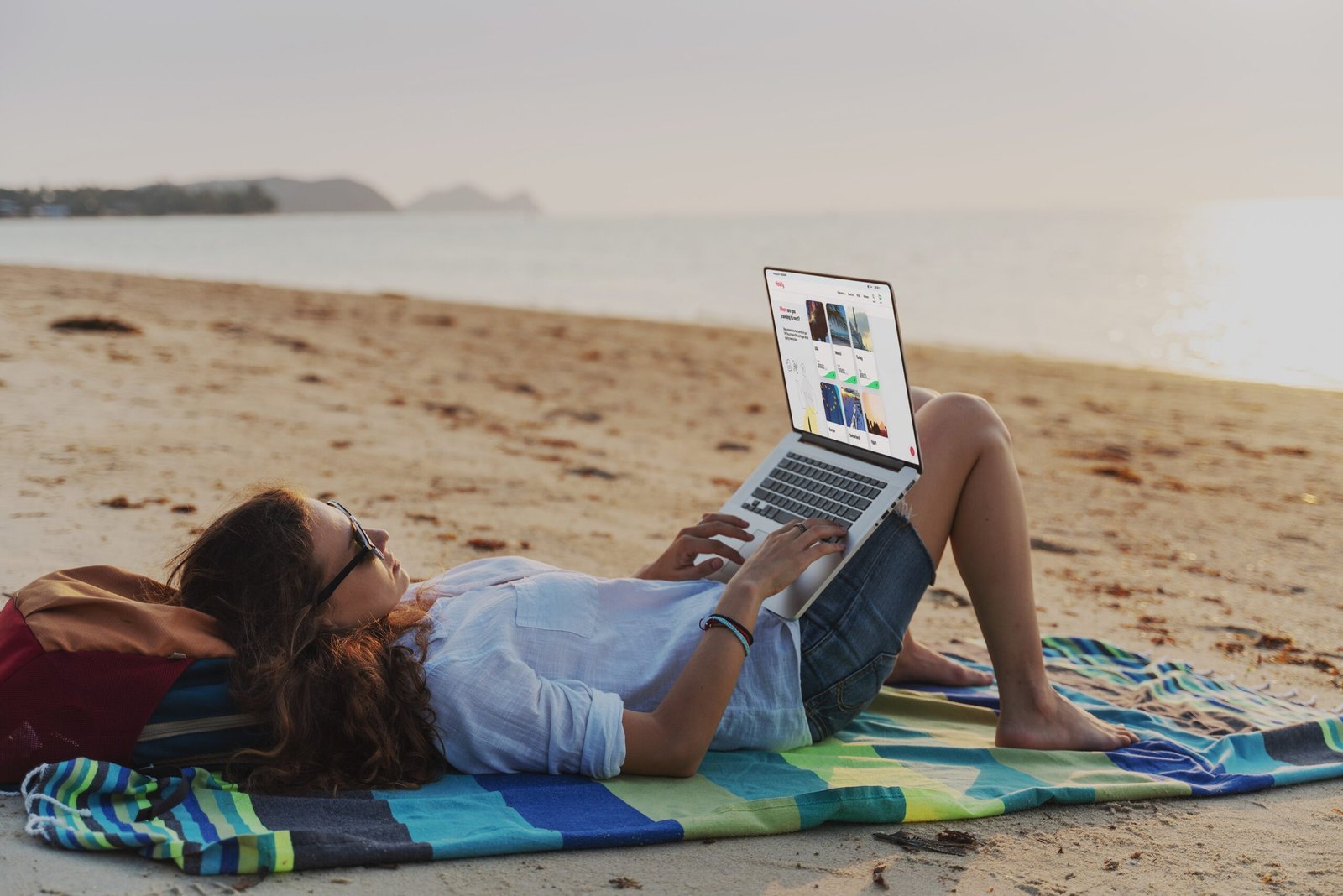 Best eSIM for International Travel (Unlimited Data + No Roaming Fees) 1 Holafly image of a person lying on a beach towerl working on her laptop in front of the sea thanks to her best eSIM for international travel